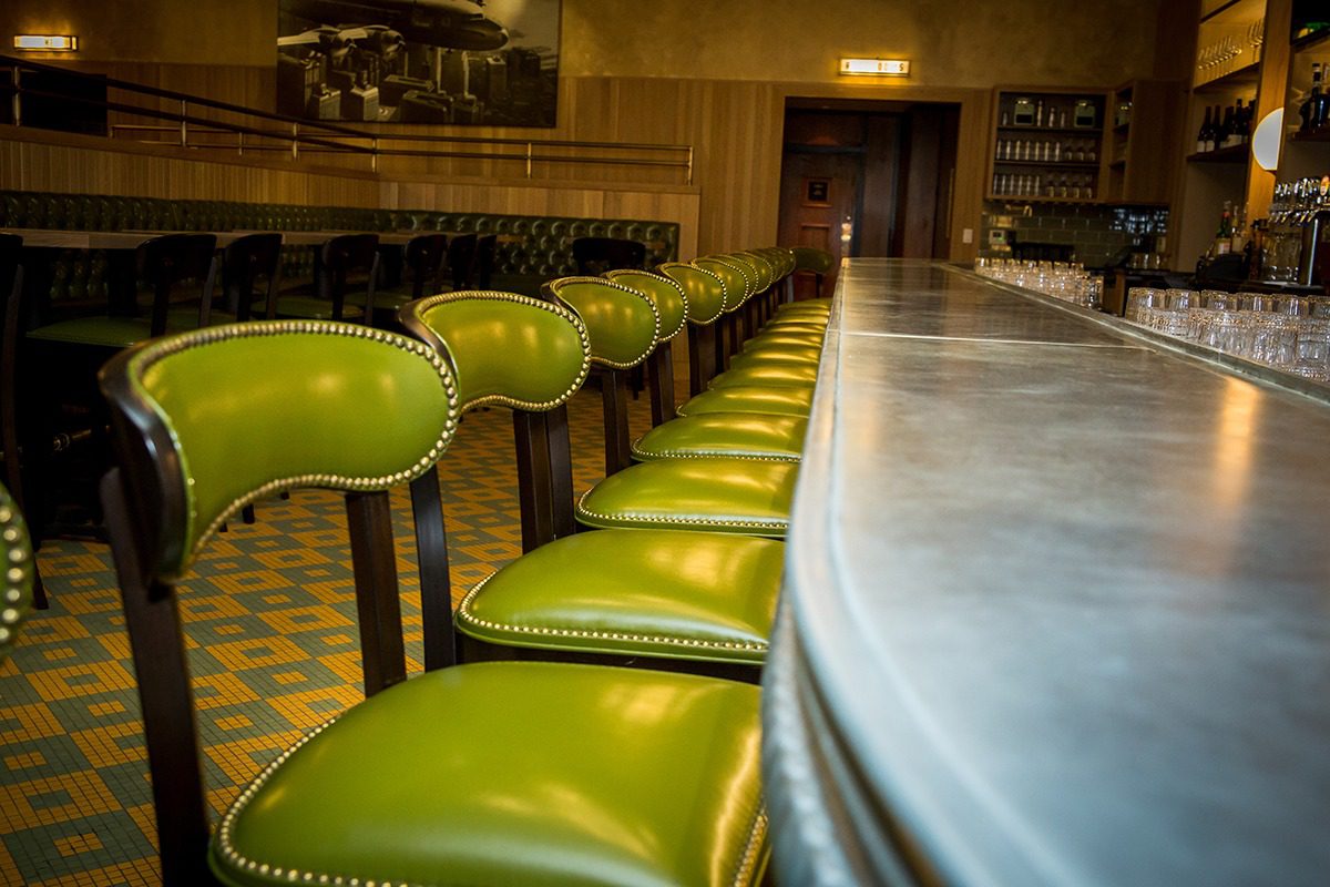 Row of green bar stools lined up along a marble countertop.