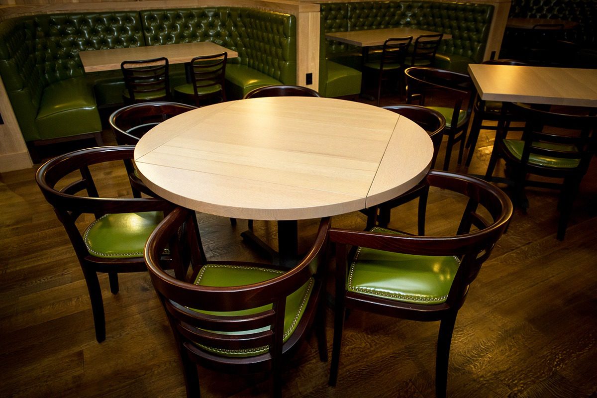 Round wooden table surrounded by green-cushioned chairs in a cozy room.