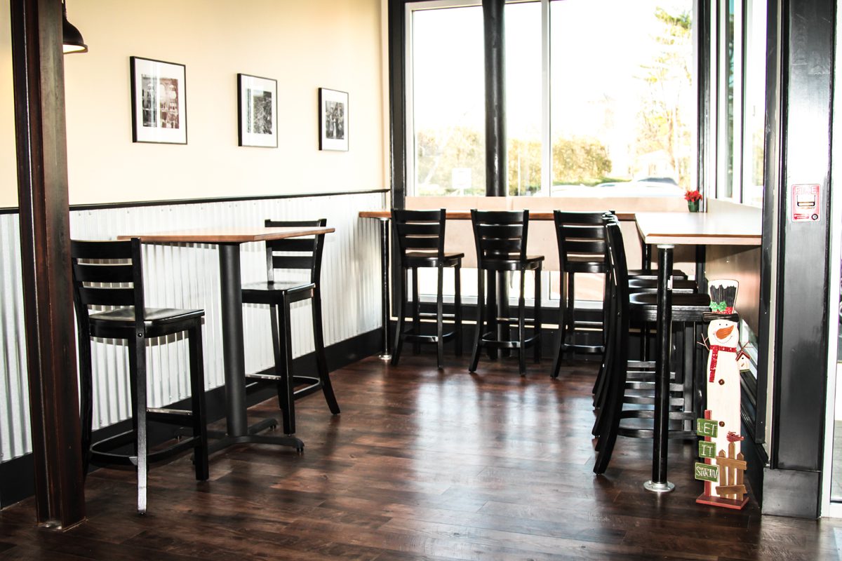 Empty cafe with wooden floors and black chairs by large windows.