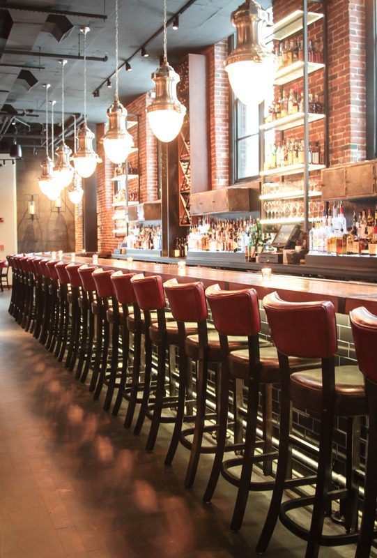 Long bar with red stools and hanging lights in a cozy setting.