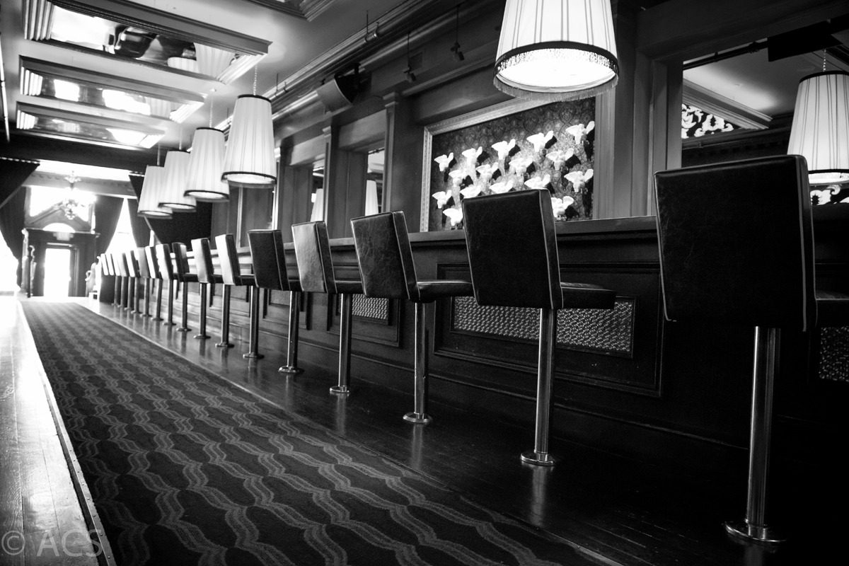 Empty bar stools lined up at a sleek bar counter in black and white.