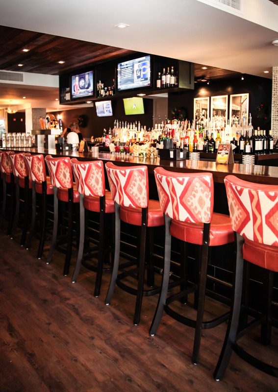 Row of red cushioned bar stools along a wooden bar counter in a cozy bar.