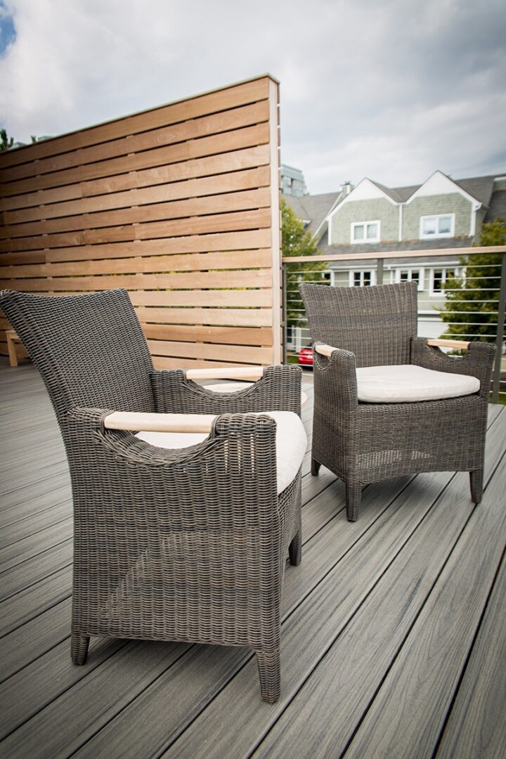 Two wicker chairs with cushions on a wooden deck near a privacy screen.