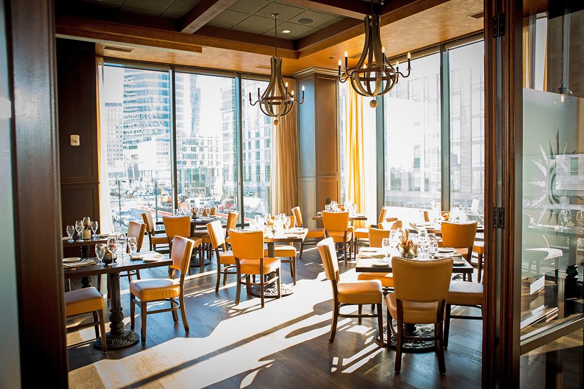 Sunlit restaurant dining area with wooden chairs and tables.