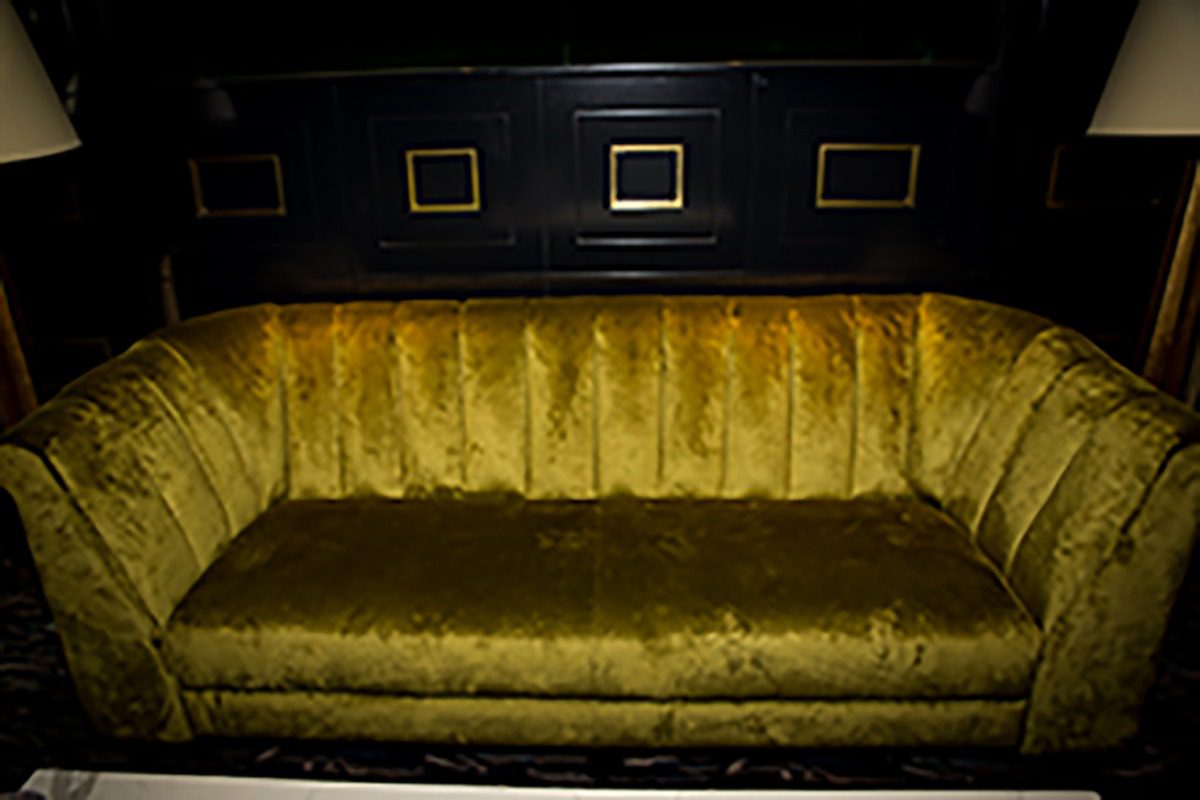 Vintage olive green velvet sofa against a dark wall.