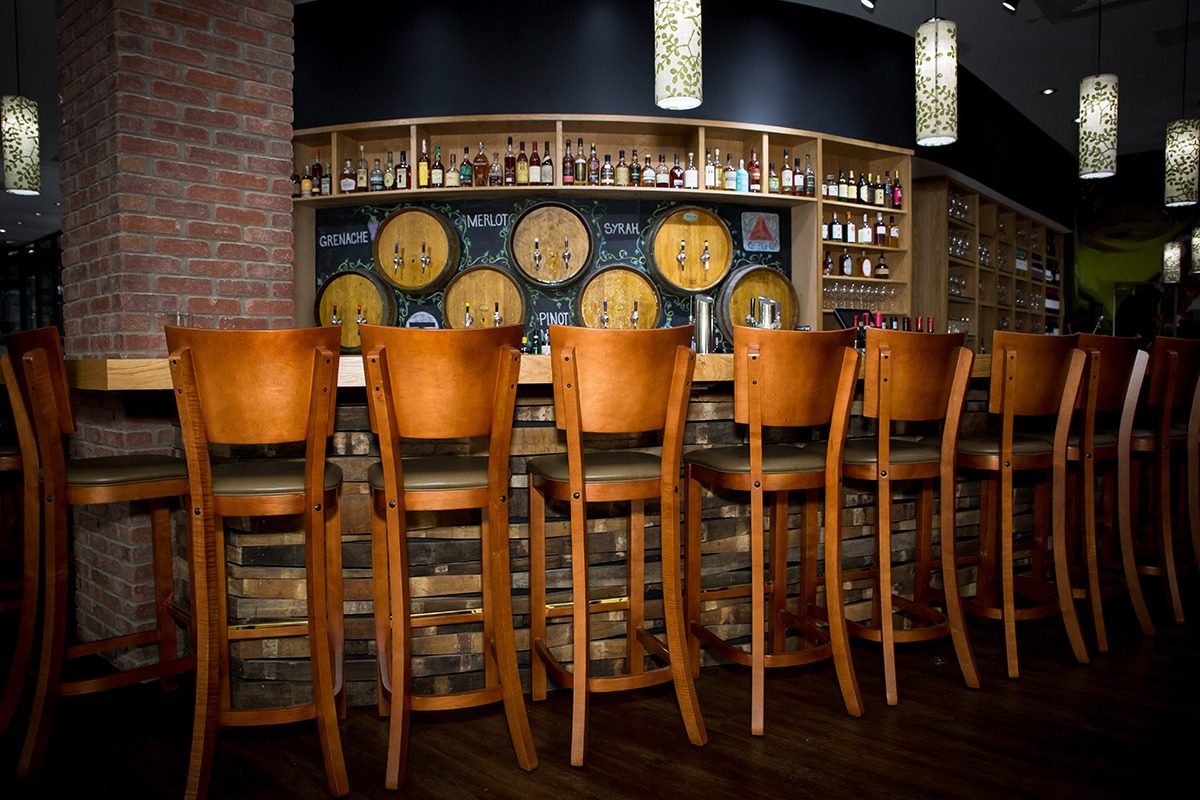 Wooden bar stools line a rustic bar with barrels and shelves in the background.