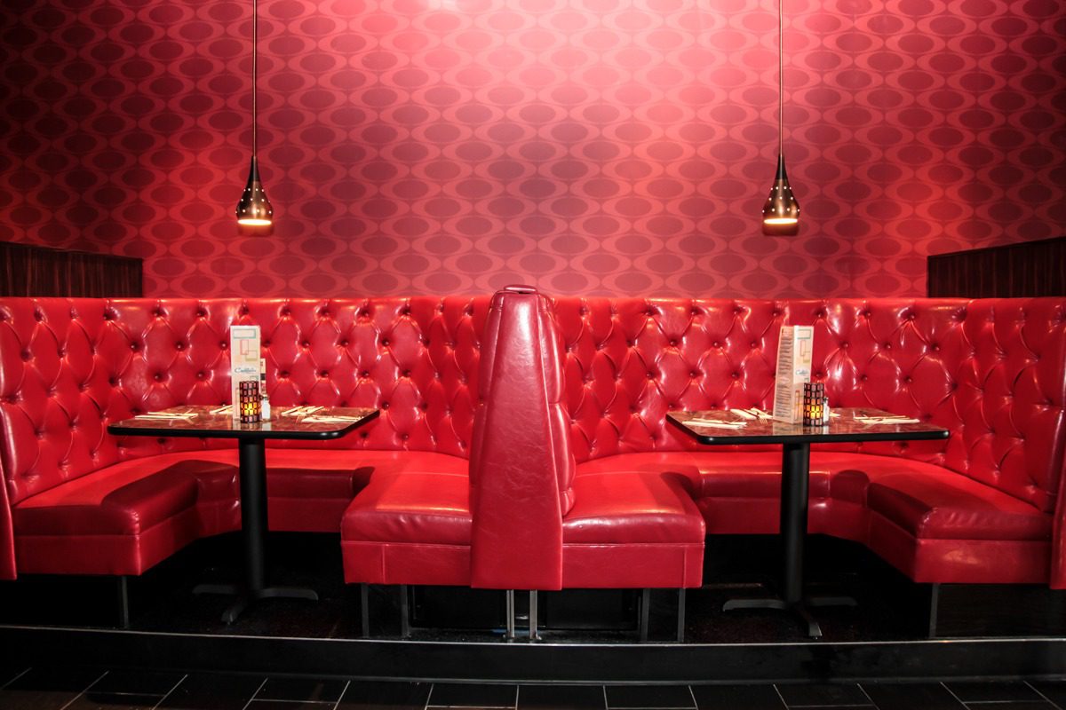 Cozy red diner booth with patterned wallpaper and pendant lights.