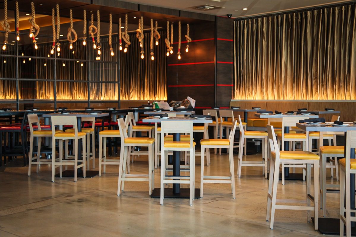 Modern restaurant interior with wooden tables and hanging lights.