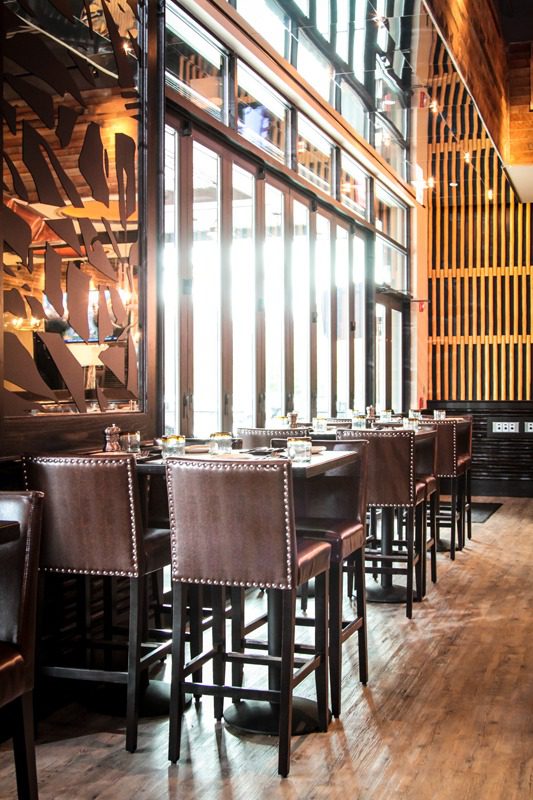 Modern restaurant interior with tall chairs and large windows.