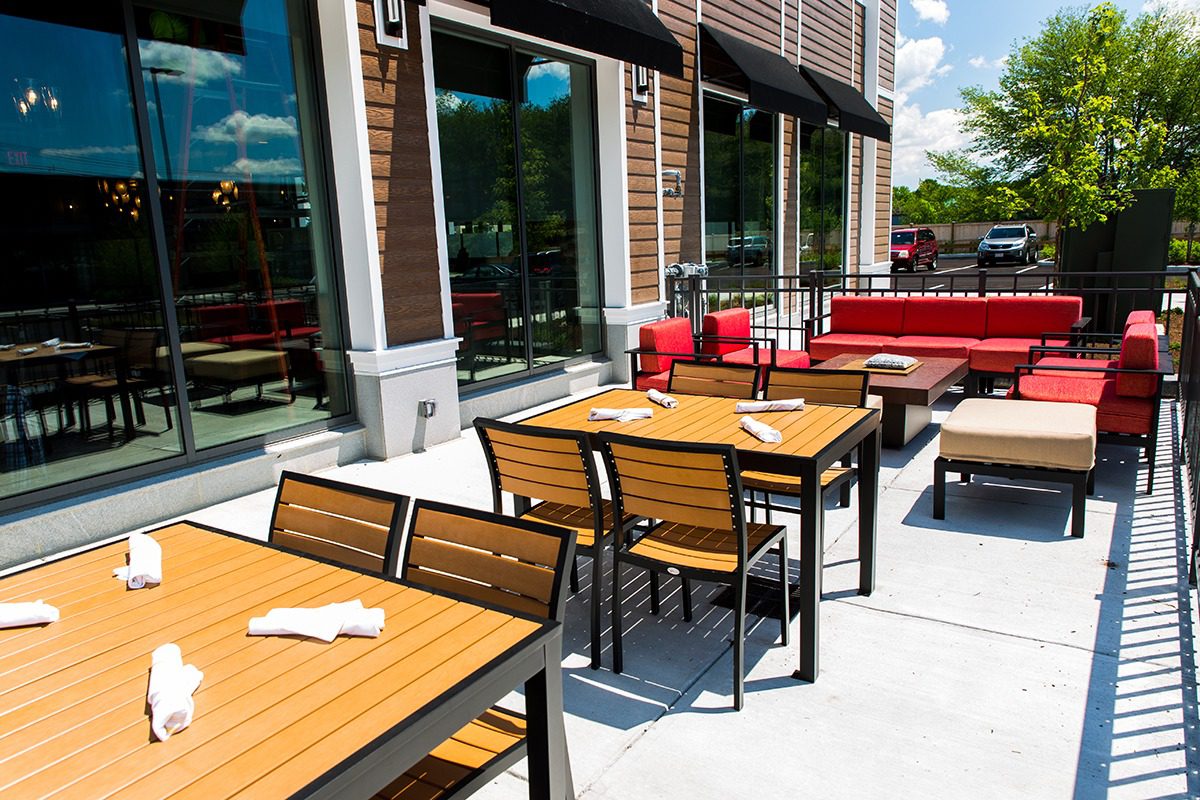 Outdoor restaurant seating with wooden tables and red cushioned benches.