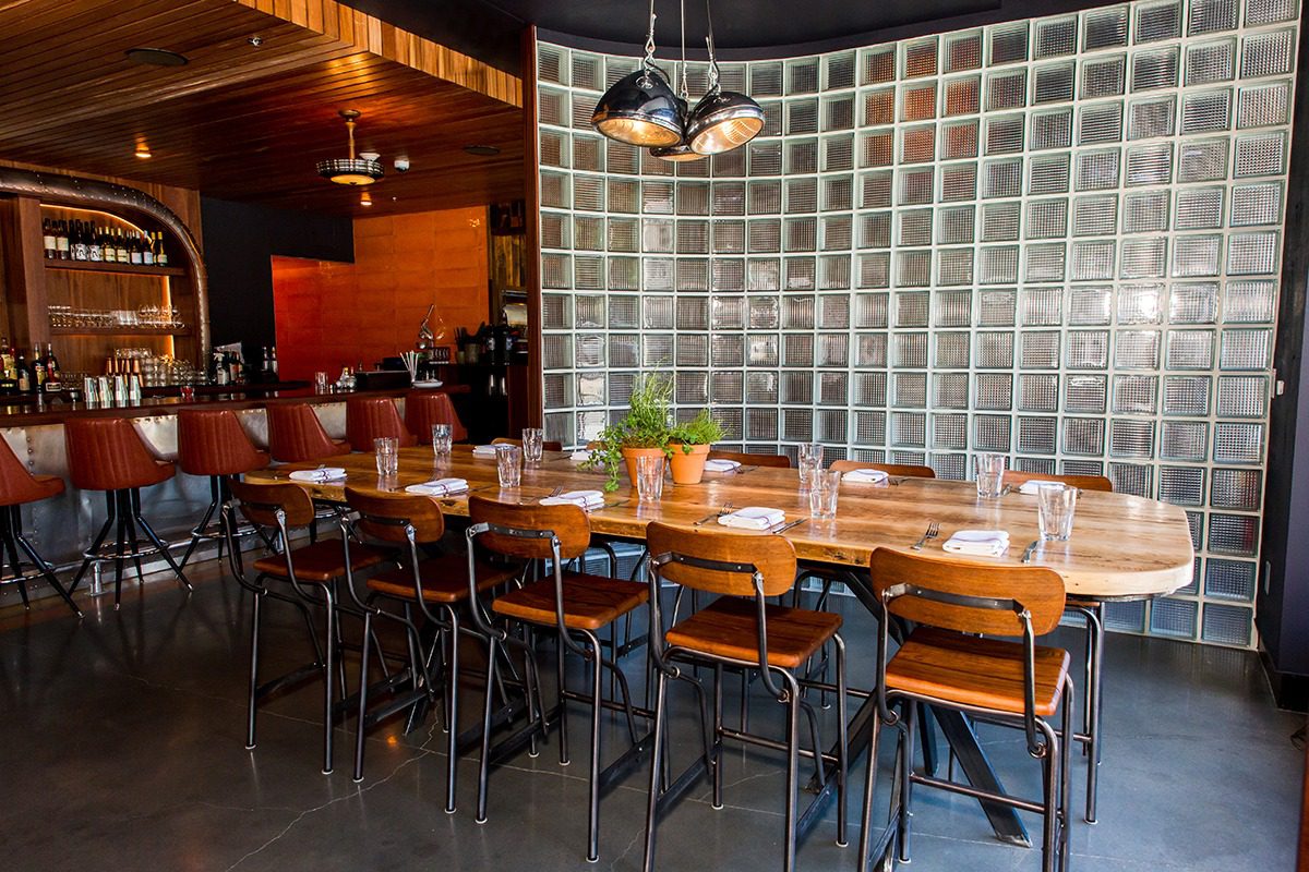 Modern restaurant interior with wooden tables and black chairs.