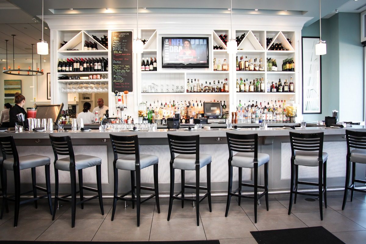 Modern bar with high stools and shelves of liquor bottles.