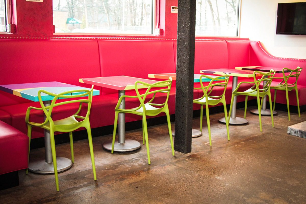 Bright green chairs with red cushions at red tables in a modern cafe seating area.