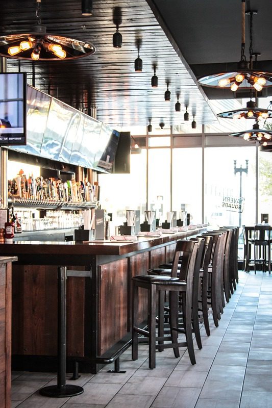 Empty wooden bar with high stools and TV screens.