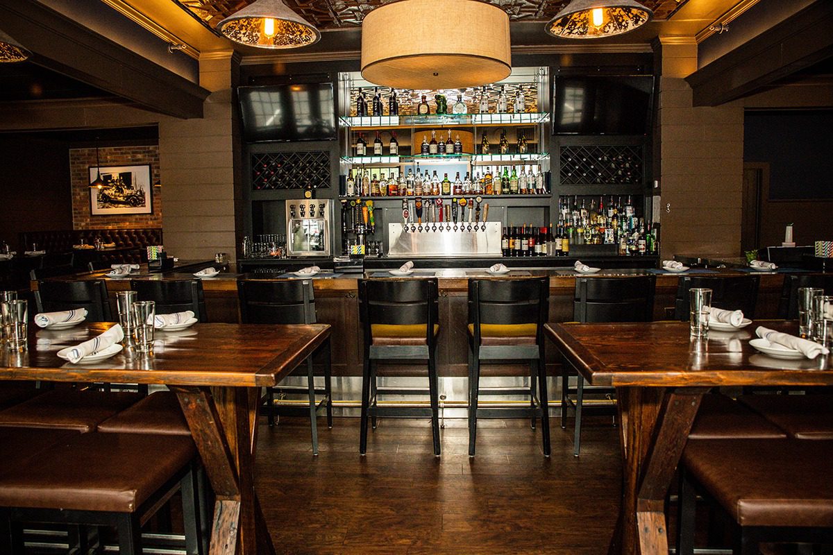 Cozy bar interior with wooden tables and stools under warm lighting.