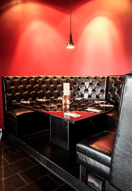 Cozy black leather booth seating with a red backdrop and a hanging light.