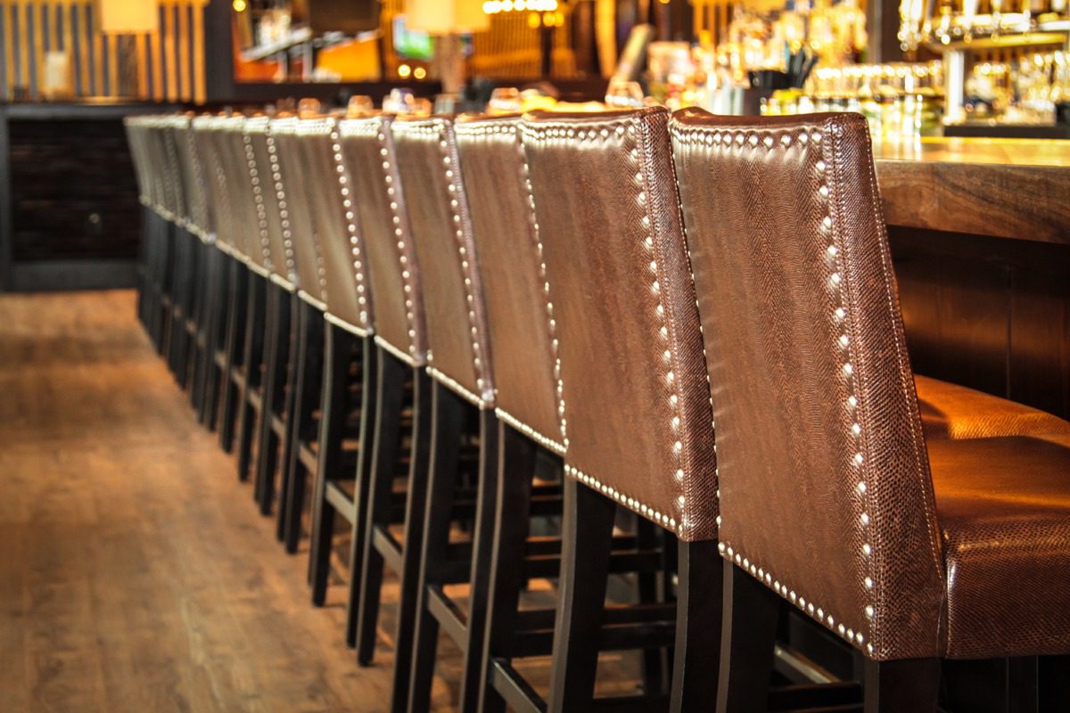 Row of brown leather bar stools lined up at a wooden counter.