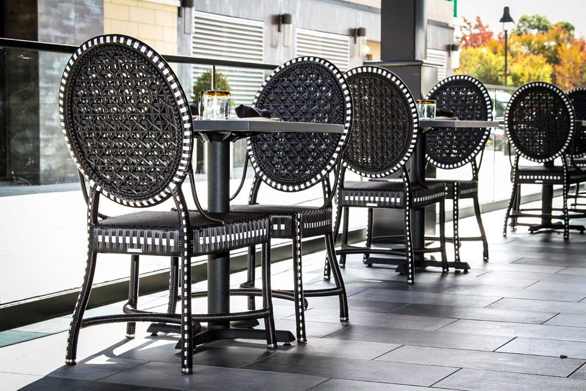 Woven black chairs and tables arranged in an outdoor dining area.