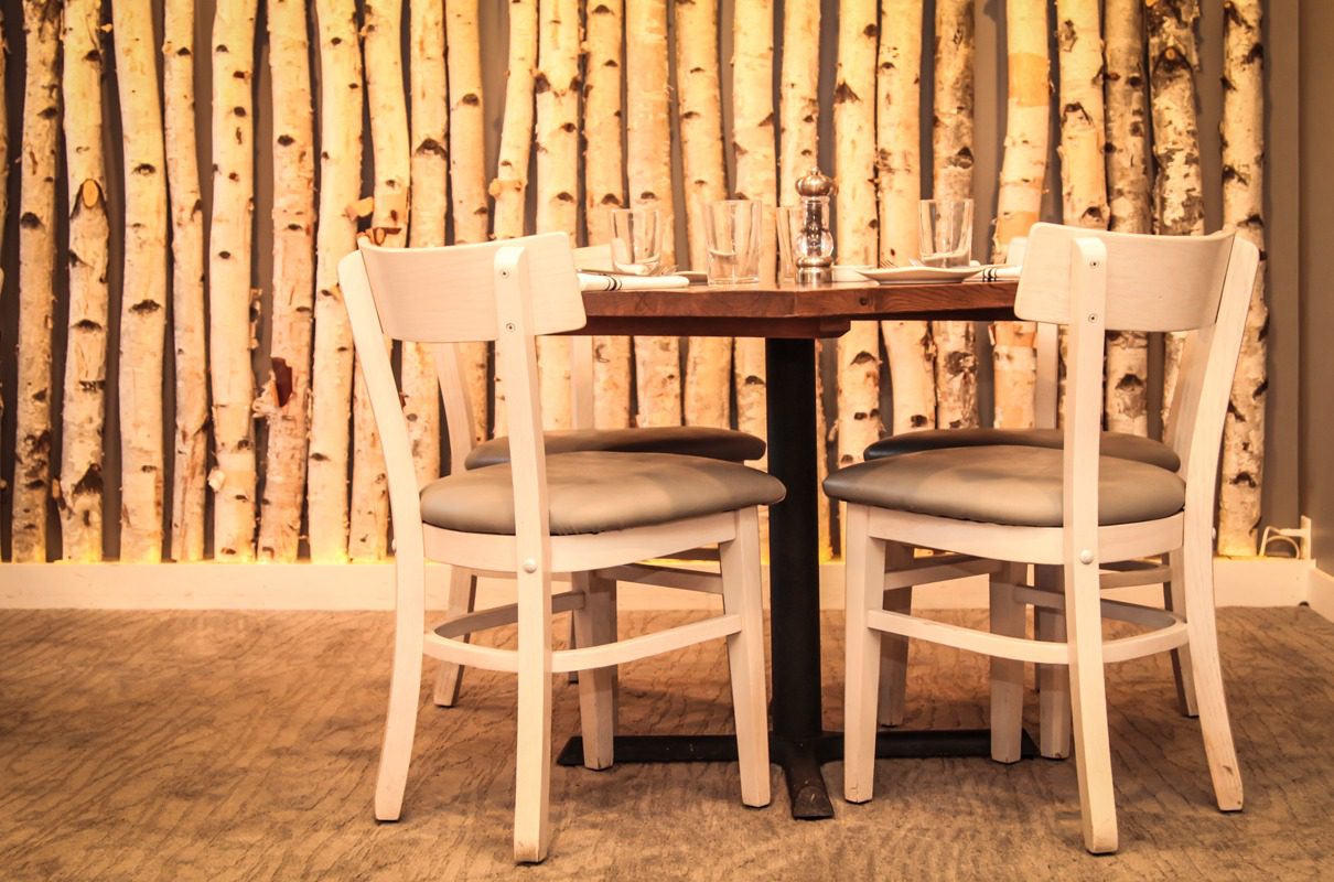 Wooden table with two chairs in front of a birch log wall.