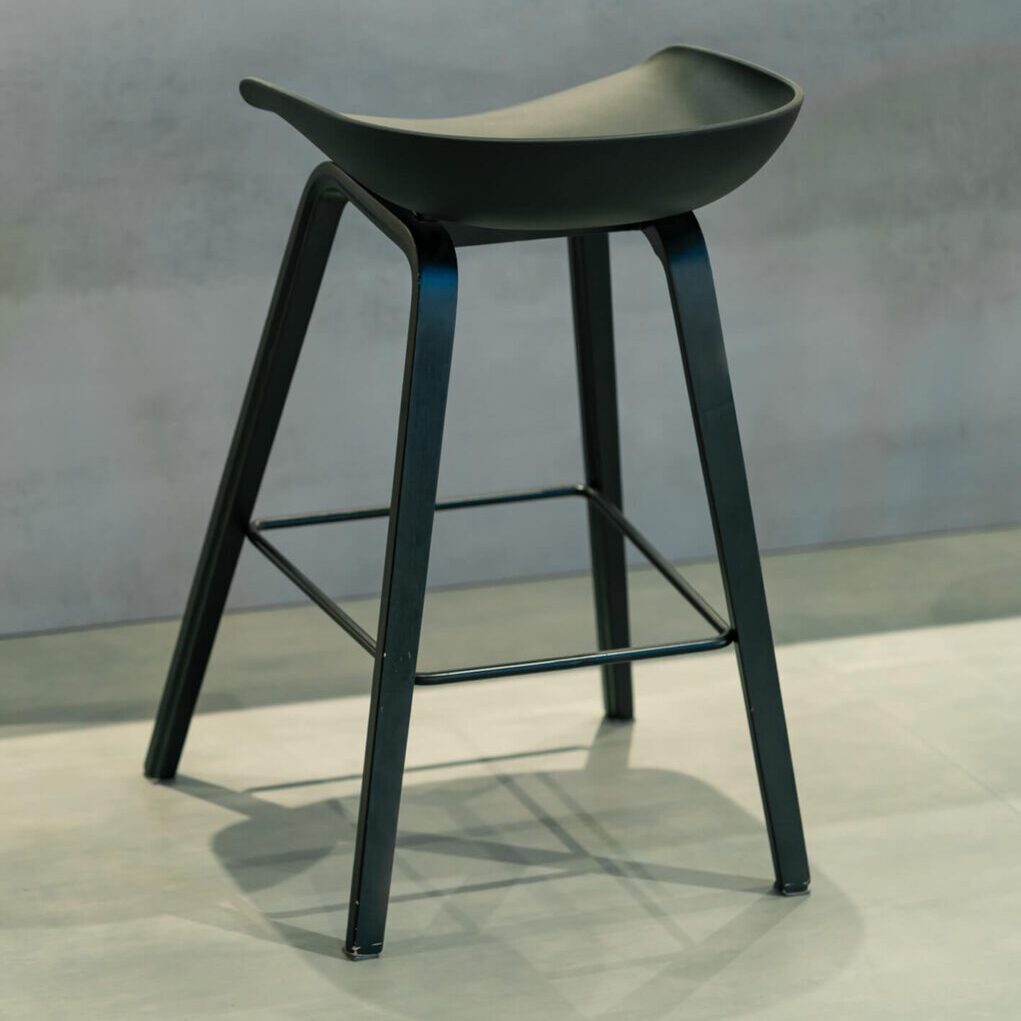 Modern black bar stool with a curved seat and four legs.