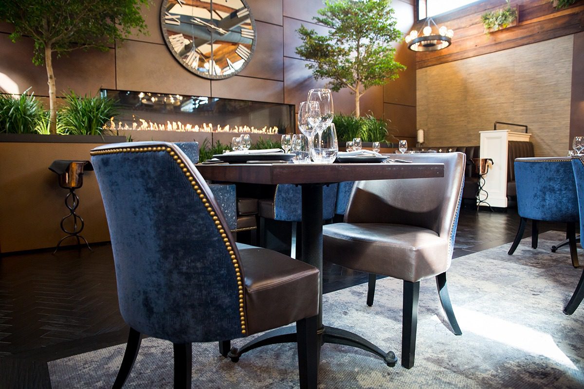 Cozy dining area with elegant chairs and a table set near a tall fireplace.