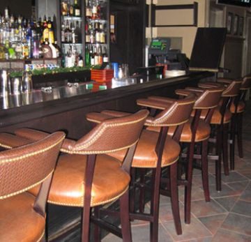 Empty bar with leather chairs and a variety of bottles on shelves.