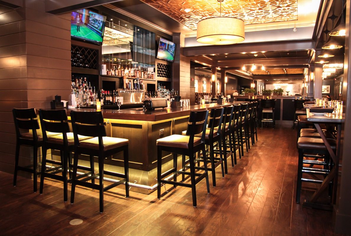 Elegant bar with wooden stools and warm lighting.