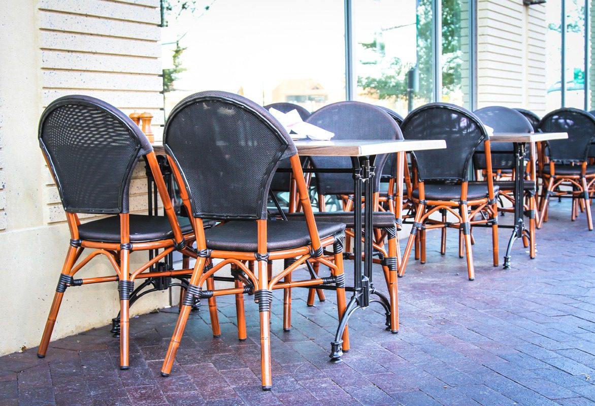 Empty outdoor cafe seating with black woven chairs and wooden frames.