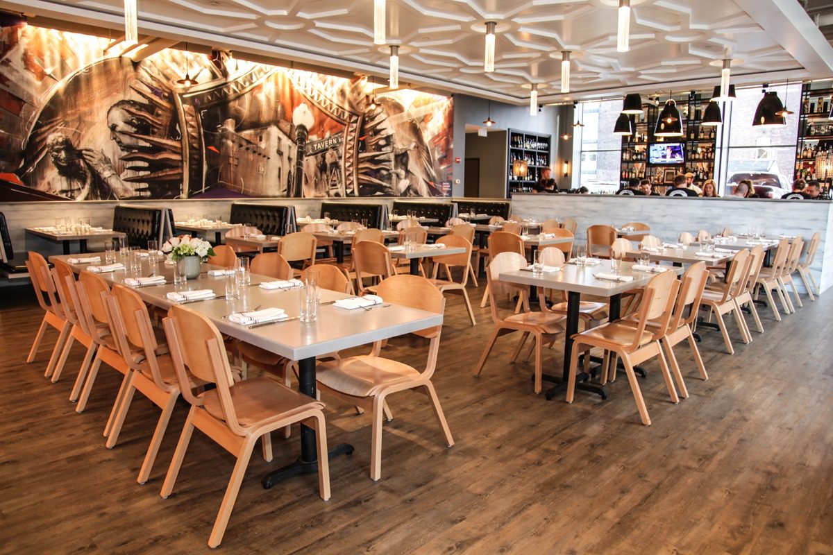 Modern restaurant interior with wooden tables and chairs, warm lighting, and a stone accent wall.