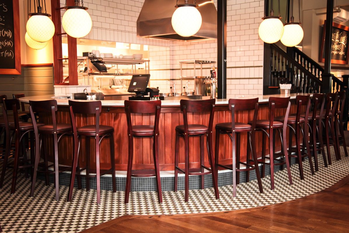 Cozy bar interior with wooden stools and warm lighting.