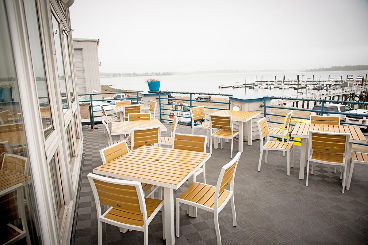Empty outdoor dining area with wooden tables and chairs overlooking the water.