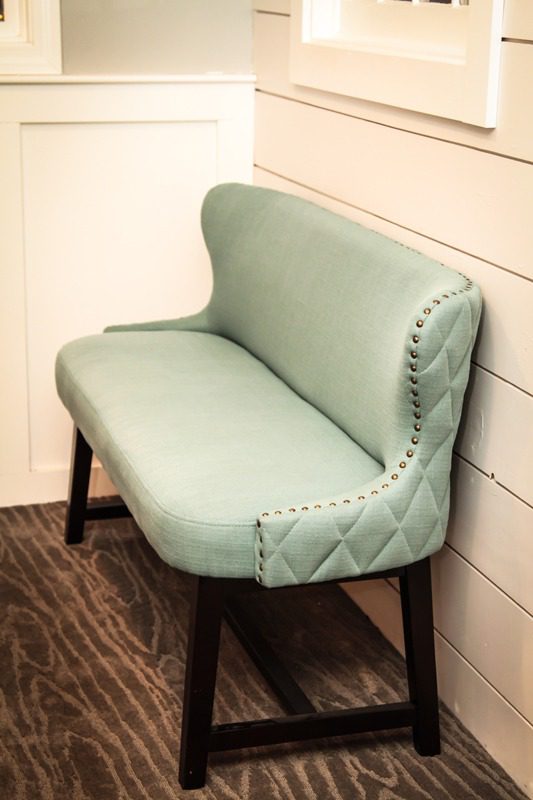 A mint green upholstered bench with wooden legs against a wall.