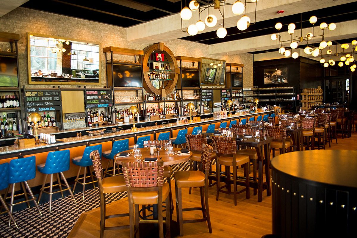 Cozy bar with wooden tables and blue bar stools under warm lighting.