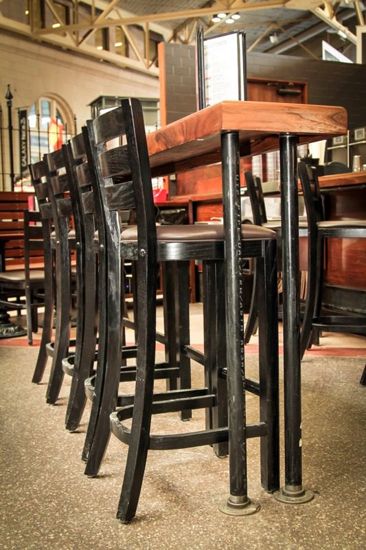 Row of tall wooden bar stools with black legs and brown seats.