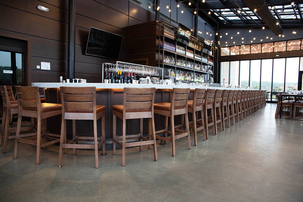 Long wooden bar with many chairs and shelves of bottles behind it.