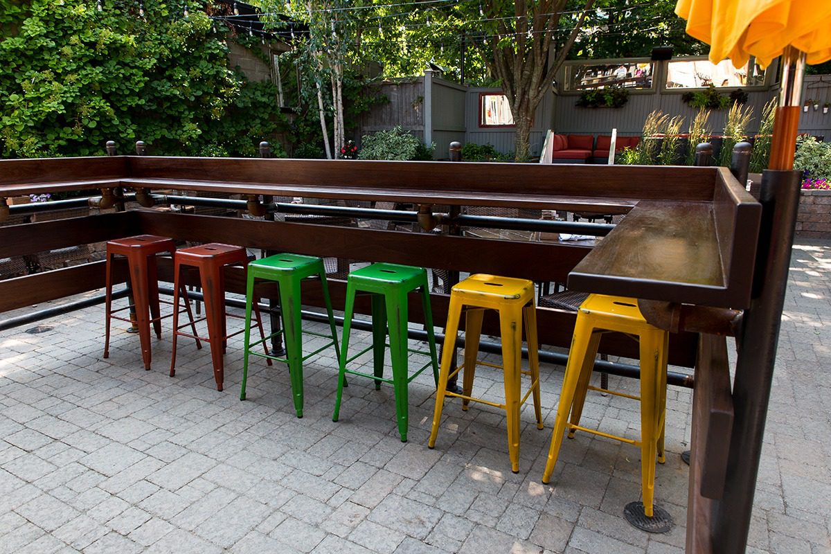 Colorful bar stools lined up at an outdoor wooden counter.