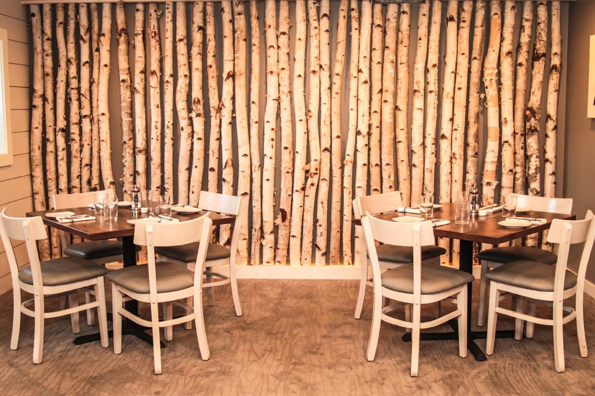 Cozy dining area with wooden chairs and birch log wall decor.