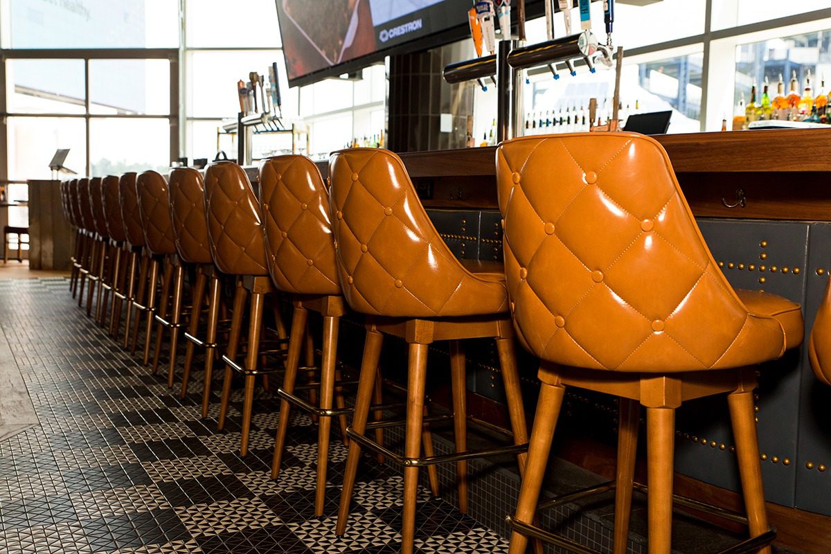 Row of orange tufted bar stools at a counter in a cozy bar.