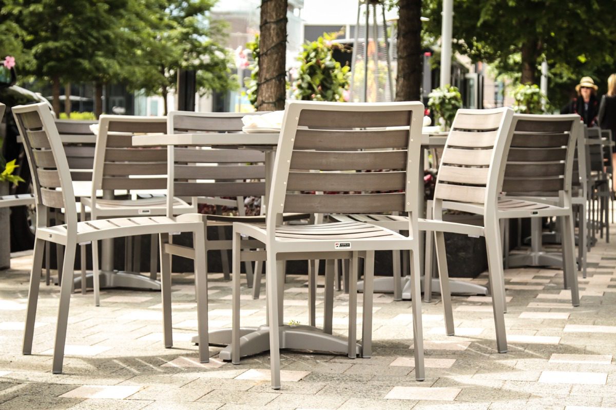 Outdoor dining area with empty wooden chairs and tables on a sunny day.