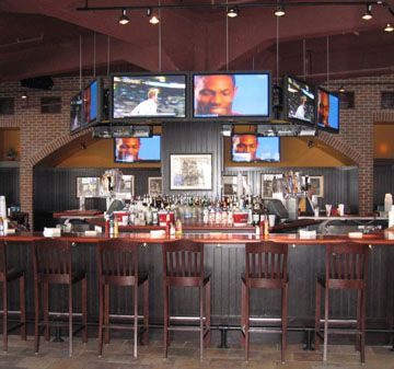 Modern sports bar with multiple TVs and wooden bar stools.