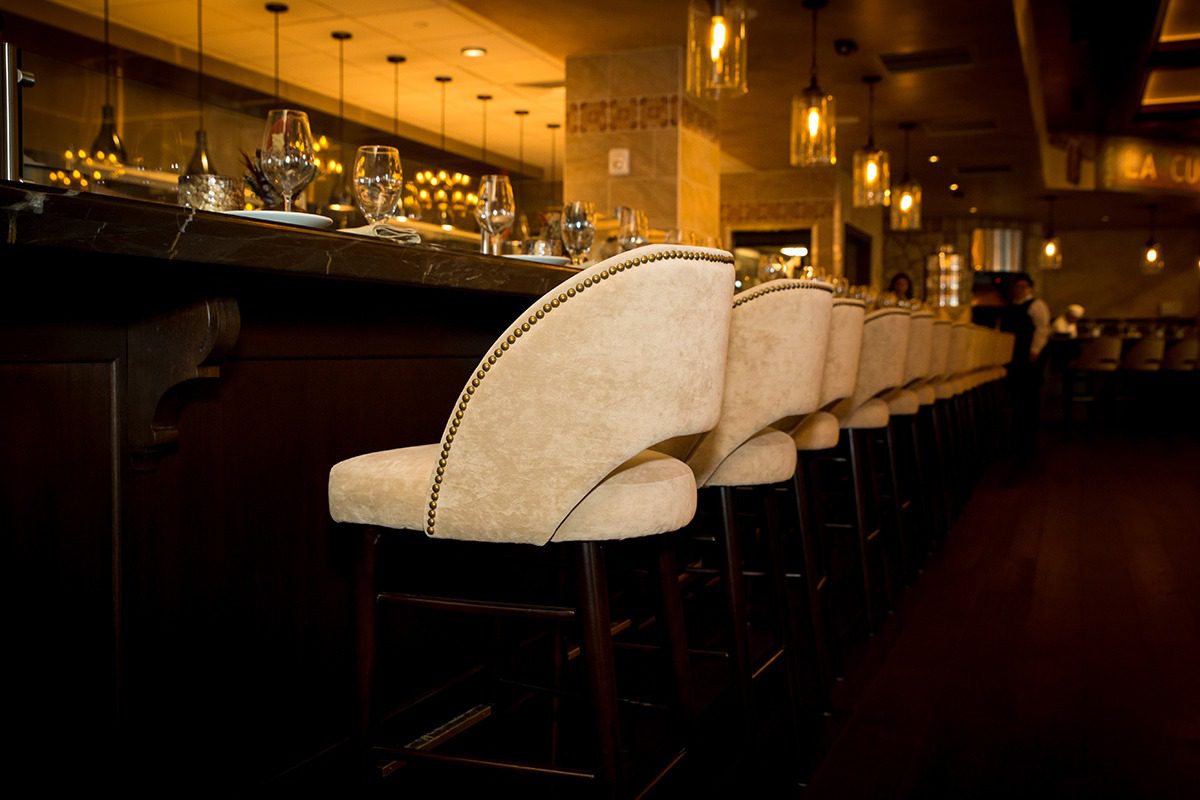 Elegant bar stools lined up along a polished wooden bar in a warm, cozy setting.