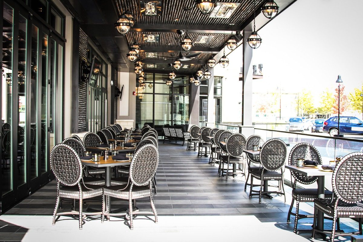 Empty outdoor café seating with elegant chairs and hanging lights.