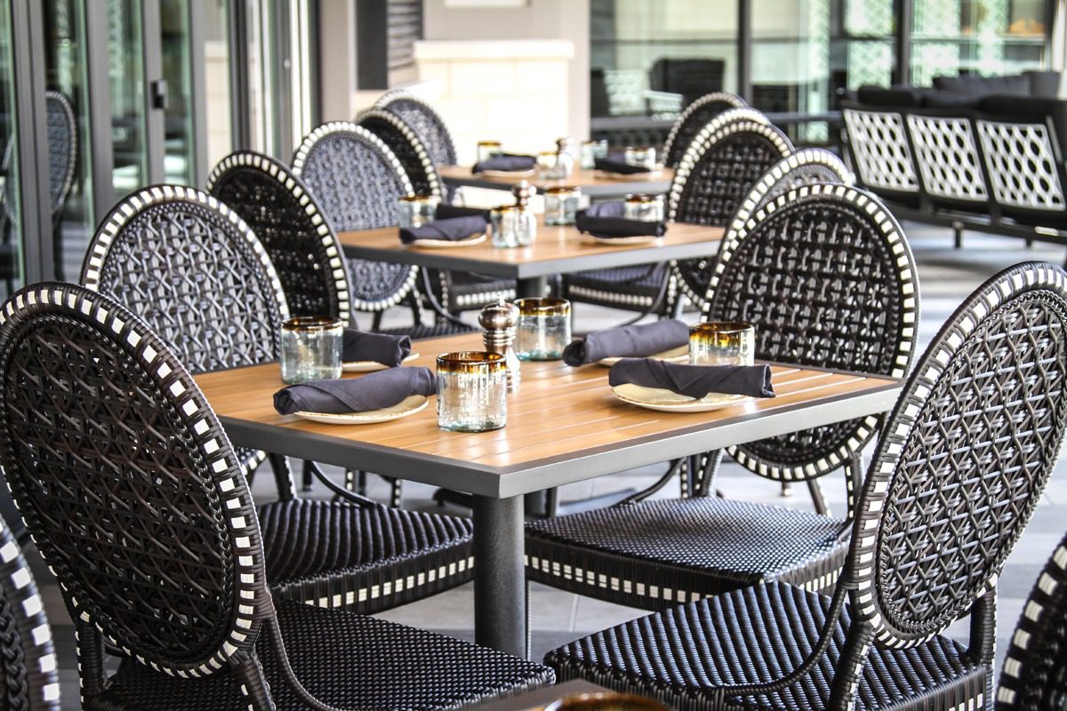 Elegant outdoor dining area with wooden tables and woven chairs.