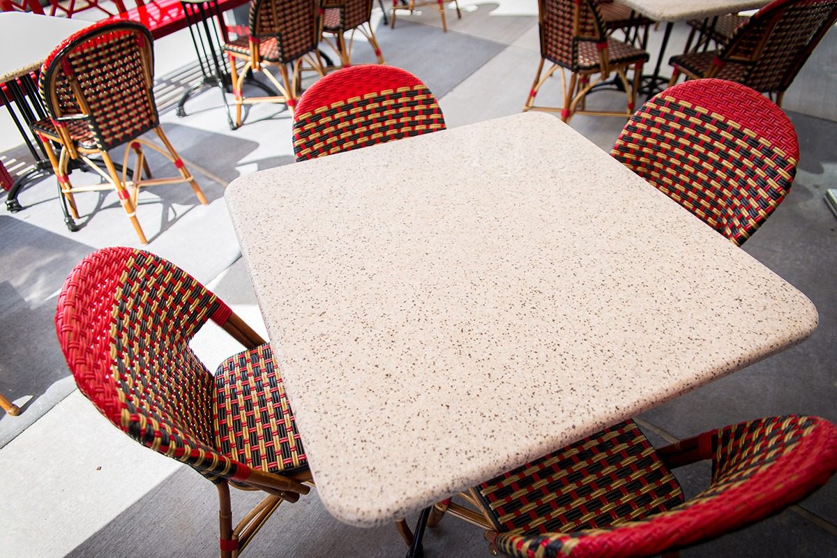 Square outdoor table with red checkered chairs in a sunny cafe.