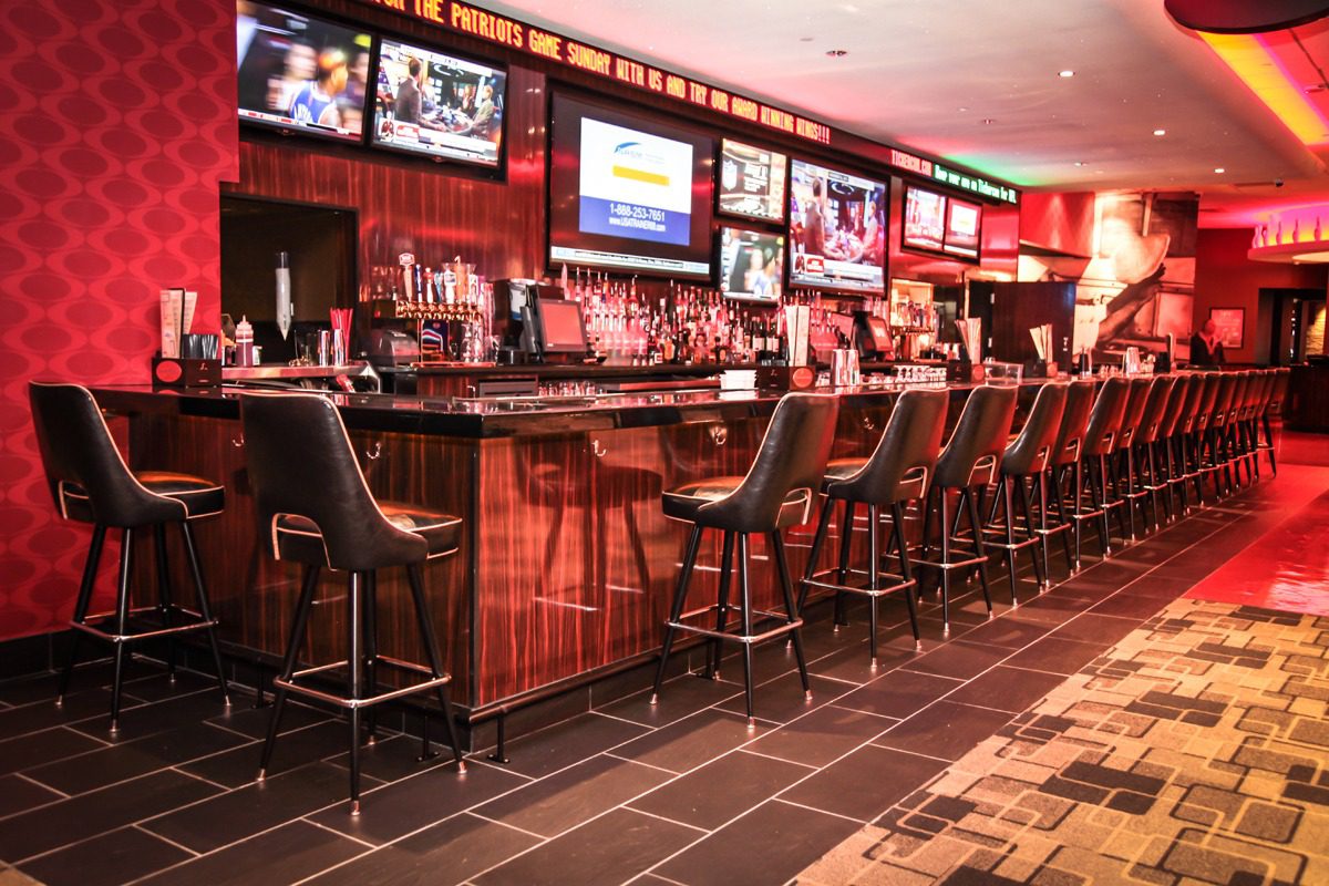 Empty bar with high stools and multiple TV screens showing sports.