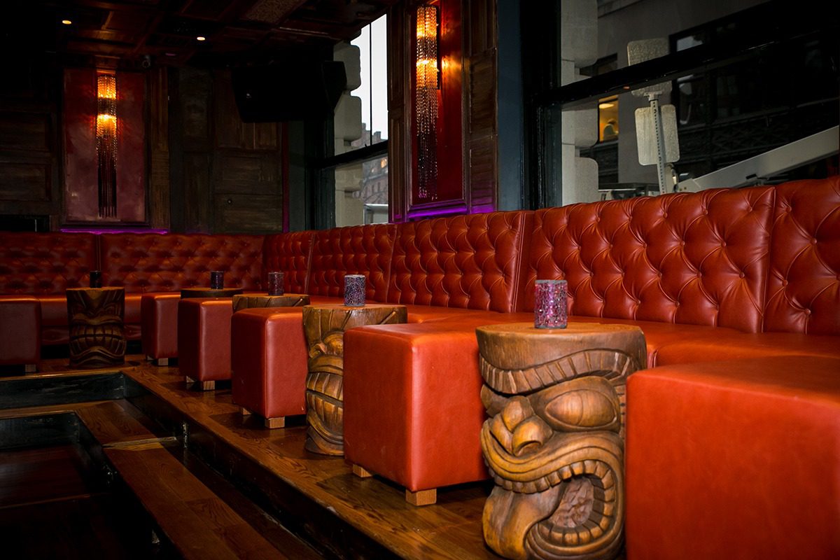 Cozy bar seating with tufted orange leather chairs and tiki decor.
