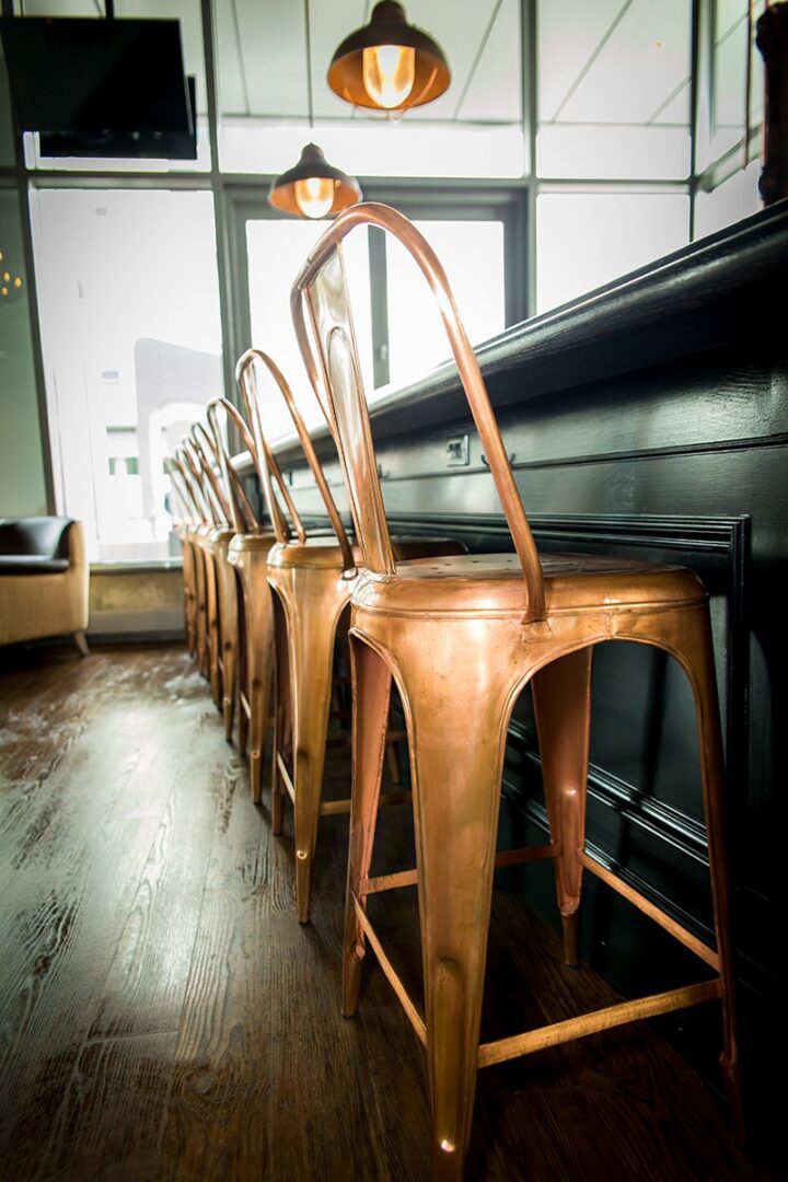 Rustic metal bar stools lined up along a wooden floor bar counter.