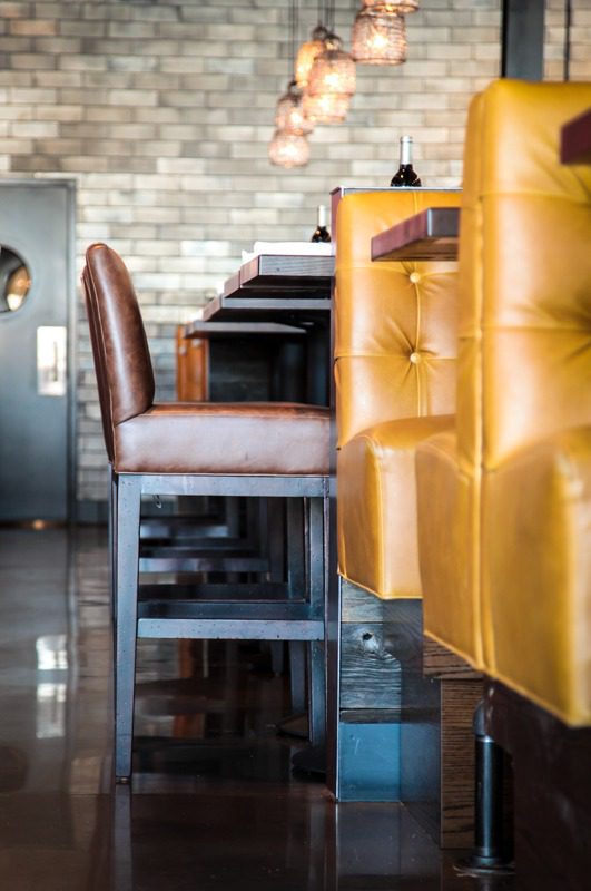 A cozy bar area with brown leather stools and mustard yellow seats.