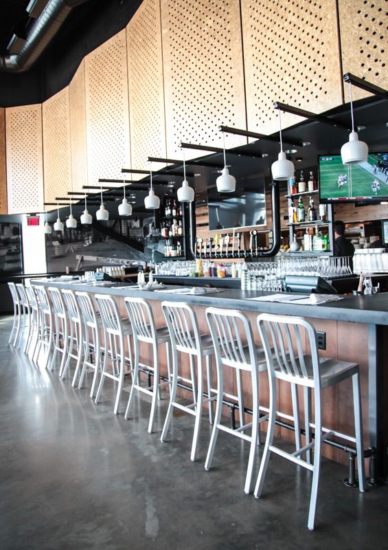 Modern bar with lined-up chairs and hanging lights.