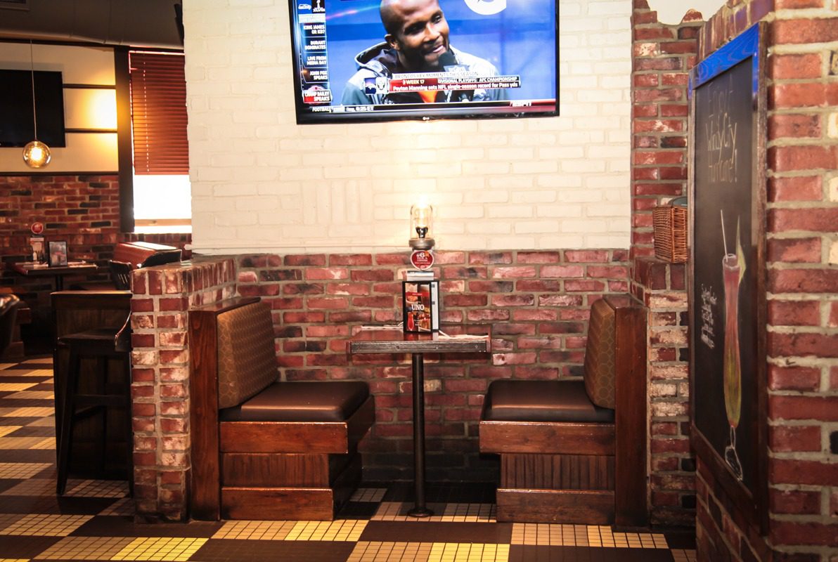 Cozy brick-walled booth with a trophy centerpiece beneath a sports broadcast.